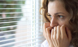 Woman looking out window, appearing worried.
