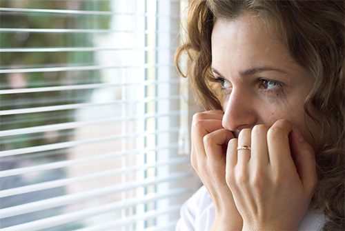 Woman looking out window, appearing worried.