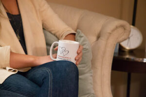 Person holding a coffee mug with a heart design, sitting comfortably on a couch.