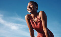A woman in athletic wear smiling joyfully outdoors under a clear blue sky.